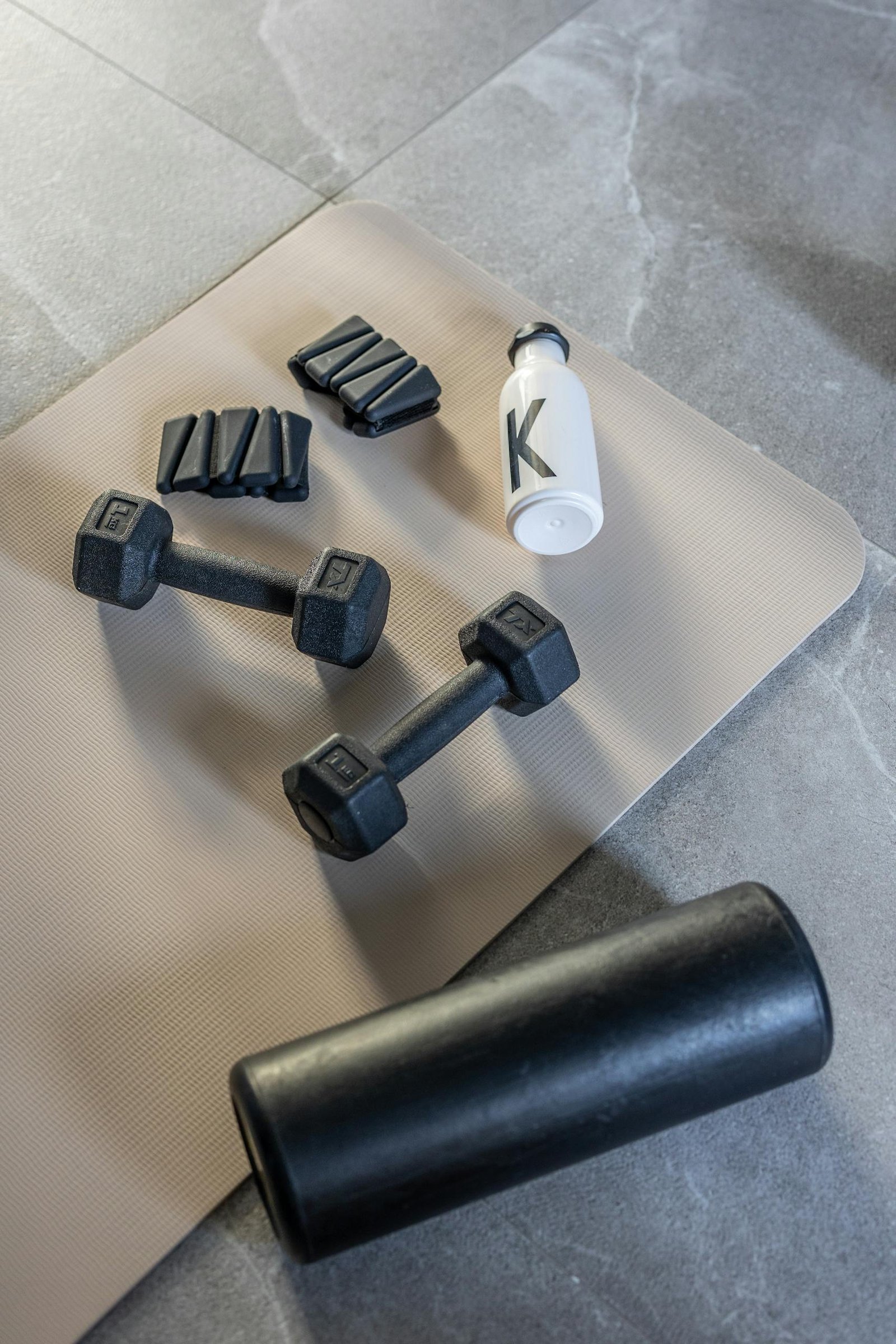 Comece Aqui Flat lay of dumbbells, weights, and bottle on mat for fitness home workout.